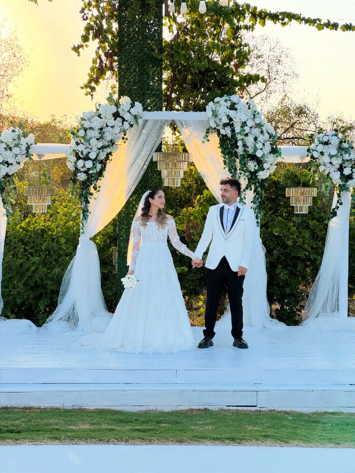 Bride and groom in front of an arch dressed in white flowers